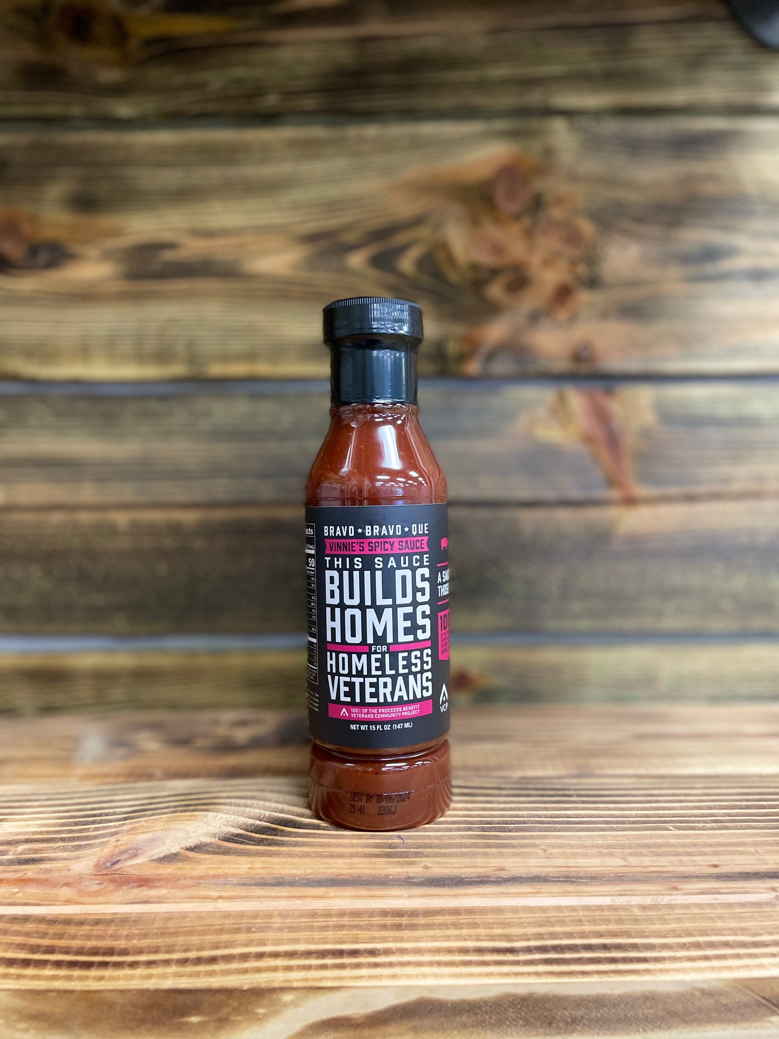 A bottle of Vinnie's Spicy Sauce on a wooden background.