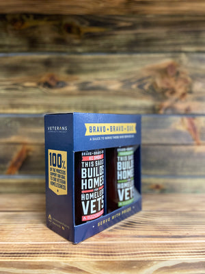 This angle shows the 100% of the proceeds support our goal to end Veteran homelessness fact on the left panel of the two bottle box with KC Smoke and Texas Black Pepper bottles in the box.