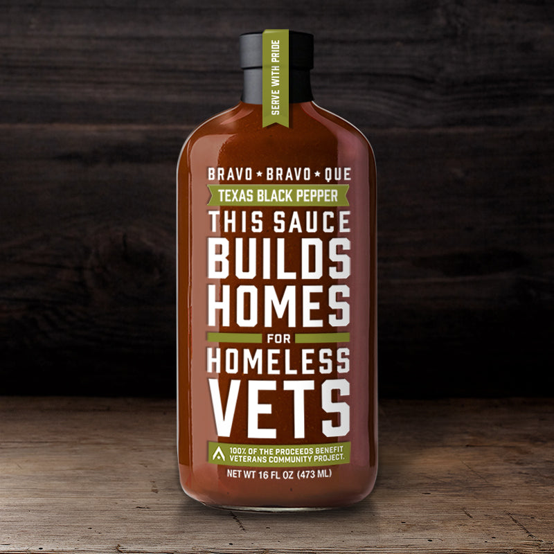 Bottle of Bravo Bravo Que Texas Black Pepper sauce on a wooden surface with a label that includes the product name and 'This sauce builds homes for homeless vets' text.